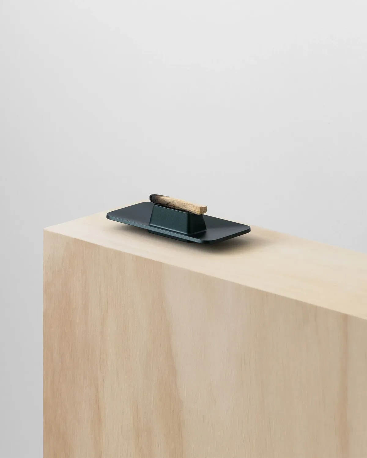 Objeto oscuro con un trozo de madera encima, sobre un bloque de madera clara